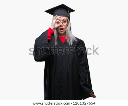Young blonde woman wearing graduate uniform over isolated background doing ok gesture shocked with surprised face, eye looking through fingers. Unbelieving expression.