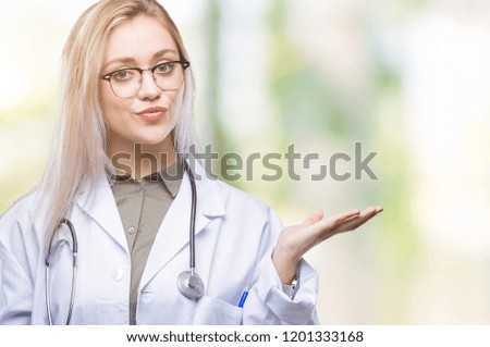 Young blonde doctor woman over isolated background smiling cheerful presenting and pointing with palm of hand looking at the camera.