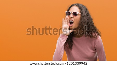 Beautiful young hispanic woman wearing sunglasses shouting and screaming loud to side with hand on mouth. Communication concept.