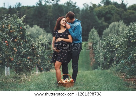 Happy healthy pregnancy and parenting. Portrait of pregnant young brunette Caucasian woman with husband on apple farm. Beautiful expecting mother and future father at countryside, rustic style
