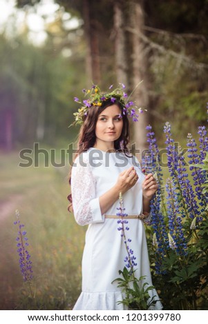 cute young girl with long hair with a wreath of flowers on her head stands in the field in beautiful colors