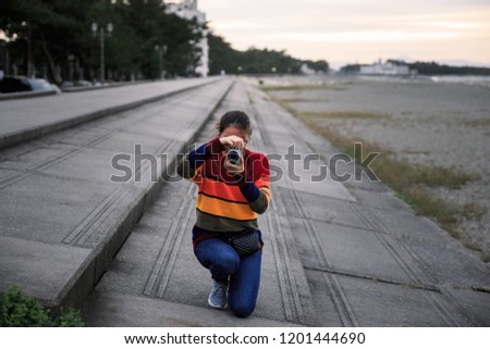 Girl crouching on concrete steps to take picture at sunset