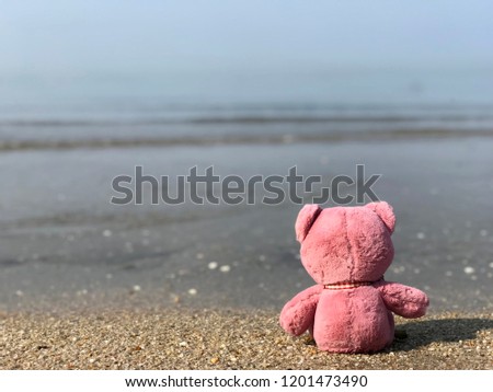 Pink teddy bear sitting lonely on the beach background. Waiting or missing someone concept