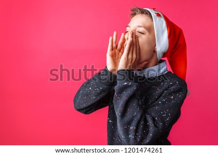 Beautiful teen, in Santa hat, in winter clothes, screaming, Christmas theme isolated on red background