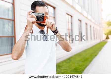 Stylish hipster with a camera, taking pictures, walking around the city in a good mood