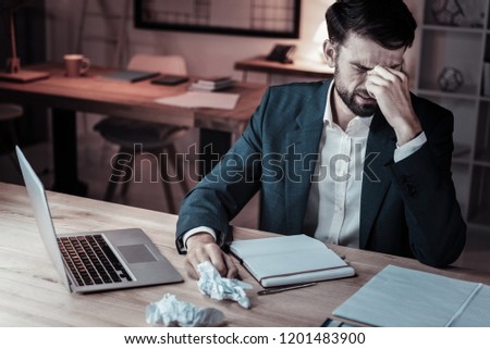  Concentrated male person leaning arms on the table and bowing head while touching bridge of his nose