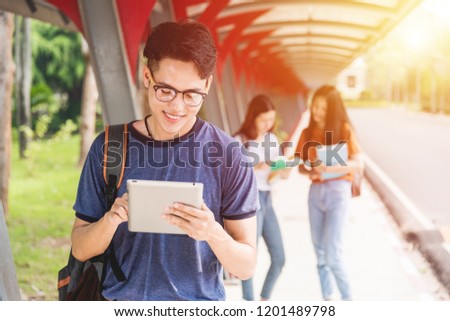 Asian Male student using tablet computer to reads information at school campus. There are groups of man and girlfriends behind, Education back to university concept