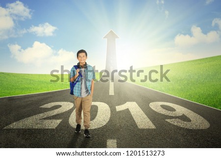Picture of preteen boy student smiling at the camera while walking above number 2019 on the road with upward arrow