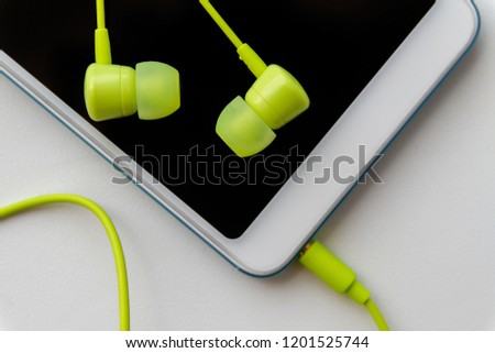 Modern smartphone with lime headphones on light background. Closeup, selective focus