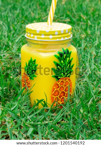 Mug with straw and juice with a pattern of pineapple. On the background of green grass.