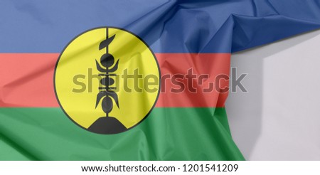 New Caledonia fabric flag crepe and crease with white space, blue red and green with a yellow disc fibrated black and defaced with a vertical symbol, also black.