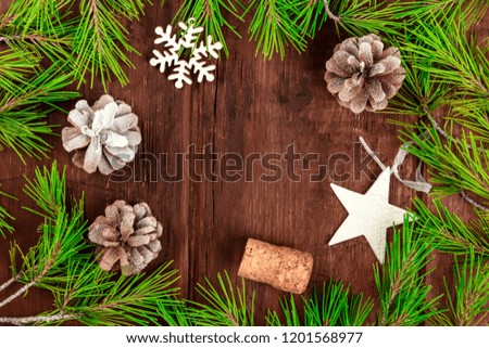 Christmas background with fir tree branches, cones, snow, xmas decorations, and a champagne cork, on a dark rustic texture with copy space