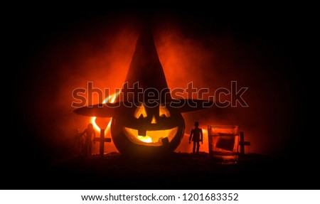 Halloween pumpkin with carved face and glass of whiskey with ice on a dark toned foggy background with zombies. Decorated. Selective focus