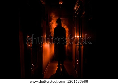 Creepy silhouette in the dark abandoned building. Horror Halloween concept. Dark corridor with silhouette of horror person standing in center. Toned light and fog on background.
