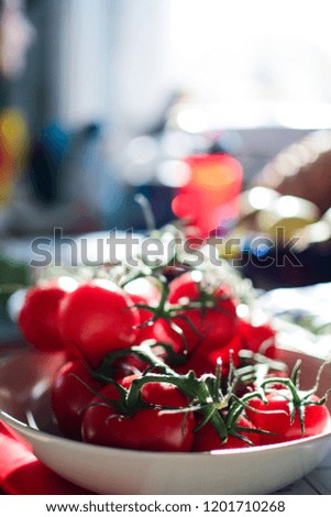 Concept of vegan food, selective focus. An organic red tomato in a white ceramic pot on a kitchen counter near the window. Natural light blurred background. Vertical.