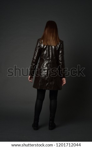 full length portrait otfbrunette girl wearing long leather coat and boots. standing pose with back to the camera,
