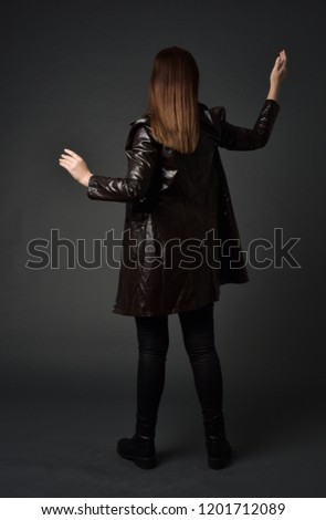 full length portrait otfbrunette girl wearing long leather coat and boots. standing pose with back to the camera,