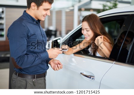 Image of loving husband giving key from a new car to his happy wife, a gift for birthday day in automobile center