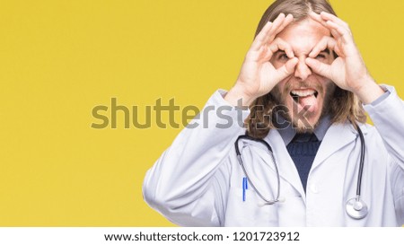 Young handsome doctor man with long hair over isolated background doing ok gesture like binoculars sticking tongue out, eyes looking through fingers. Crazy expression.