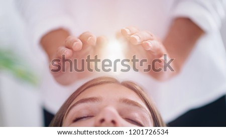 Close up image of relaxed young woman lying with her eyes closed and having Reiki healing treatment in spa center. Energy healing concept.  Royalty-Free Stock Photo #1201726534