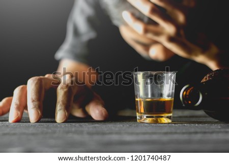 Alcohol in a small glass is placed on a black table while a man is sitting in a drunken state. Royalty-Free Stock Photo #1201740487