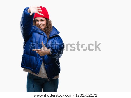 Beautiful young brunette curly hair girl wearing winter coat, wool cap and sweater over isolated background smiling making frame with hands and fingers with happy face. Creativity and photography