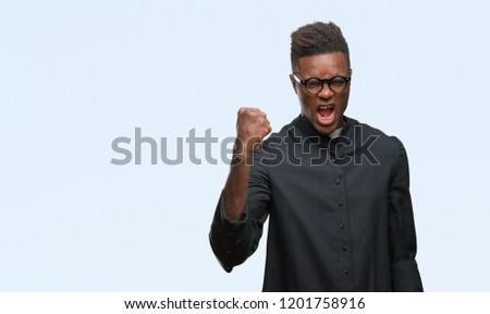 Young african american priest man over isolated background angry and mad raising fist frustrated and furious while shouting with anger. Rage and aggressive concept.