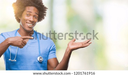 Afro american surgeon doctor man over isolated background amazed and smiling to the camera while presenting with hand and pointing with finger.
