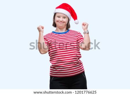 Young adult woman with down syndrome wearing christmas hat over isolated background very happy and excited doing winner gesture with arms raised, smiling and screaming for success. Celebration concept