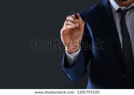 Businessman holding pen in hand on dark background