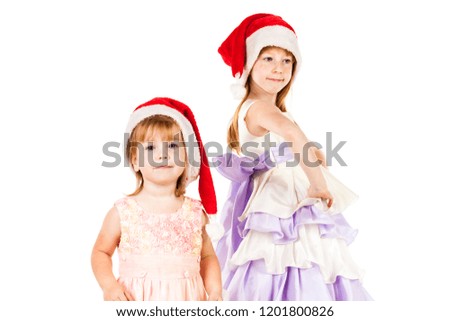 Little red haired and freckled face girl dressed in Santa's hat posing, dancing and dreams about gifts. Christmas and New Year advertising concept. Studio shoot isolated on a blurred white background