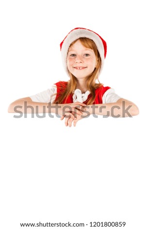 Little red haired and freckled face girl dressed in Santa's hat holds blank flipchart board and dreams about gifts. Christmas and New Year advertising concept. Isolated on a blurred white background