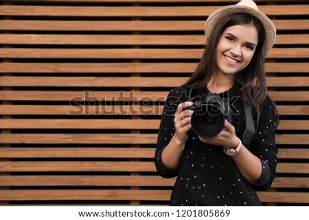 Young female photographer with professional camera near wooden wall. Space for text
