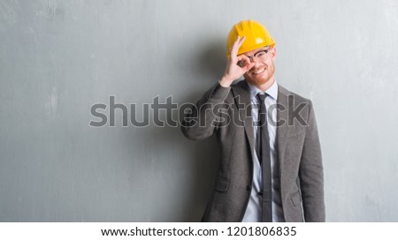 Young redhead man wearing architect outfit and helment with happy face smiling doing ok sign with hand on eye looking through fingers