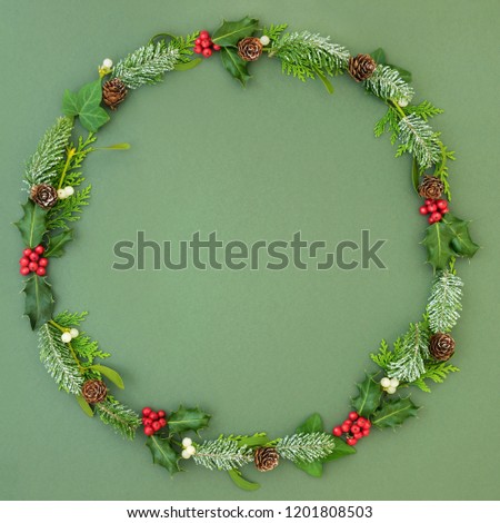 Natural winter and Christmas wreath with cedar cypress and snow covered fir leaf sprigs, holly berries, ivy and mistletoe on mottled green background. Traditional christmas card for the festive season