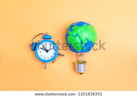 Light bulb with plasticine Earth planet model and alarm clock on yellow background. Global ecology, International Day of Energy Saving or Earth Hour concept.