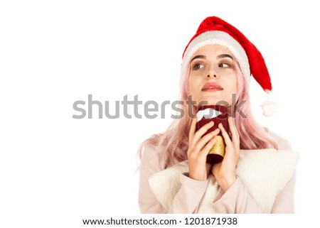 Attractive smiling young girl dressed in Santa's hat holds the colorful mug and pillow and dreams about gifts. Christmas and New Year advertising concept isolated on abstract blurred white background