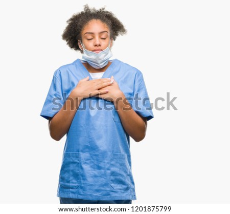 Young afro american doctor woman over isolated background smiling with hands on chest with closed eyes and grateful gesture on face. Health concept.