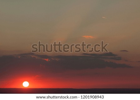 Natural sun exposure on field or meadow. Bright dramatic sky and dark earth. Countryside landscape under scenic colorful sky at sunset. Sun over the horizon. Warm colors