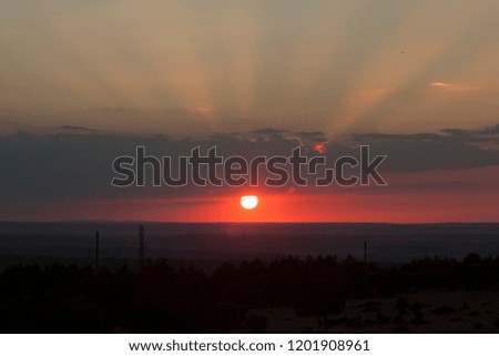 Natural sun exposure on field or meadow. Bright dramatic sky and dark earth. Countryside landscape under scenic colorful sky at sunset. Sun over the horizon. Warm colors