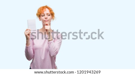 Young redhead woman holding blank notebook serious face thinking about question, very confused idea