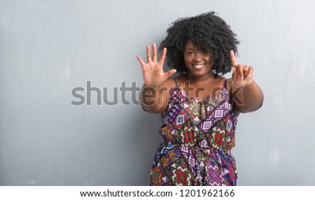Young african american woman over grey grunge wall wearing colorful dress showing and pointing up with fingers number six while smiling confident and happy.