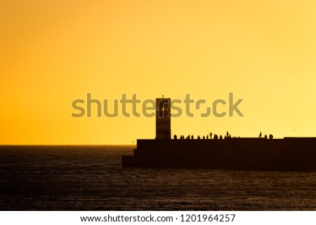 A group of people stand near a lighthouse before sunset.