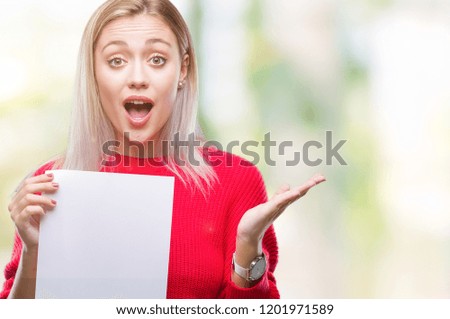 Young blonde woman holding blank paper sheet over isolated background very happy and excited, winner expression celebrating victory screaming with big smile and raised hands