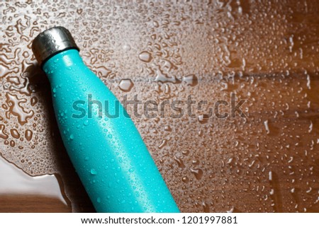 Stainless steel thermos bottle isolated on a wooden table sprayed with water. Light blue color.