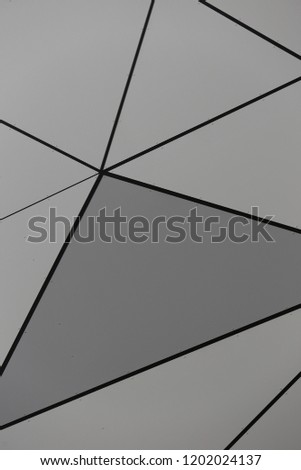 Close up outdoor view of part of a grey modern wall covered by metallic polygonal sheets. Abstract design with black lines and gray triangles. Futuristic geometric picture of a bright surface.