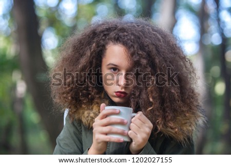 Portrait of curly hair teen girl holding mug in the park