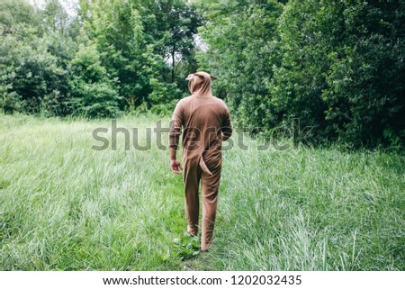 Young man is walking in the forest in cosplay costume of a cow. Guy in the funny animal pajamas sleepwear  in the nature. Halloween ideas for party.
