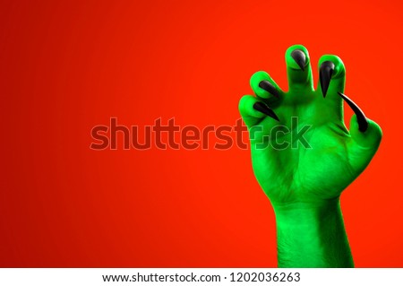 Halloween, nightmare creature and evil monster horror story concept with a scary zombie or demon hand with creepy long black nails isolated on orange background with a clip path cutout and copy space