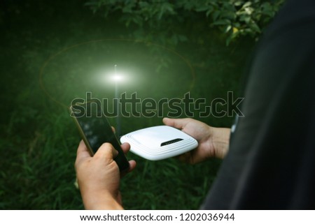 Man is looking for wi-fi signal in the nature. Guy is lost and holding router with smartphone  in his hands searching for internet connection. Modern technologies concept. Summer forest photo.